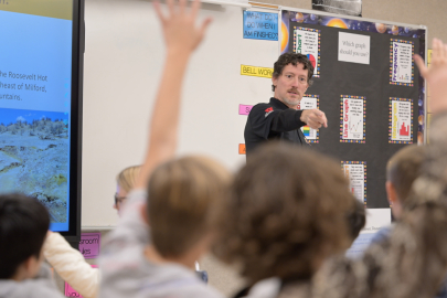Utah FORGE staff member Christopher Katis calls on one student among many raised hands in an elementary school classroom.
