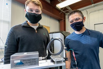 Two people, masked, standing next to research equipment