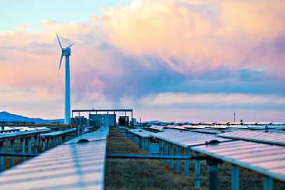 A wind turbine is seen beyond an array of solar panels.