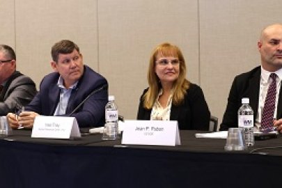 A group of panelists sitting at a table on a stage speaking into microphones 