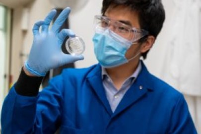 Gary holding up a pitri dish while wearing gogles, glove, mask, and lab coat