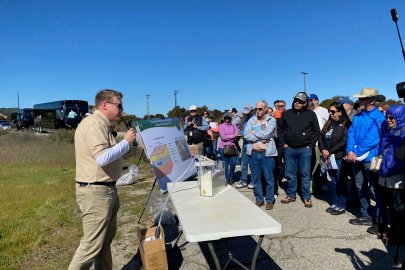 A man standing at a table with posters and science related models speaking to a crowd 