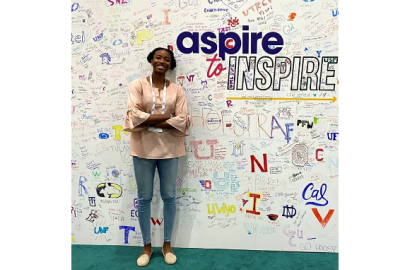 Pamela Miceus standing next to a wall of text. Largest text says "aspire to INSPIRE"