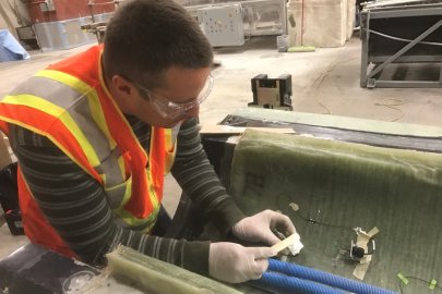 A man with safety goggles and a safety vest works on a wind turbine blade in a warehouse environment.