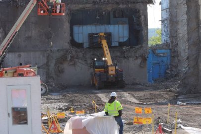 Cranes working to demolish a building, an employee in a hardhat is seen in the foreground 