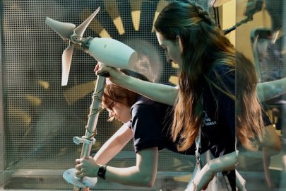 Two people setting up a wind turbine prototype inside of a wind tunnel