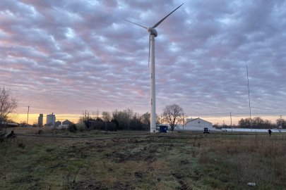 A wind turbine in field under purple hued clouds.