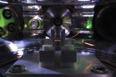 Photograph of an optically trapped microparticle in high vacuum. The microparticle is visible as a white dot levitated between two lenses, which are used to focus and collect the invisible infrared laser light used to trap the particle.