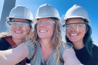 Three people are standing wearing helmets for work