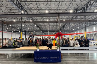 The view of the inside of a large manufacturing plant with high ceilings and a large group of workers facing the camera and smiling, with steel girders above them.
