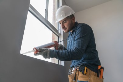A person in a hard hat and applies caulk to a window.