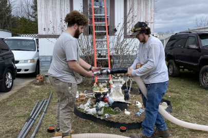 Two people hold a tube as they work in front of a mobile home.