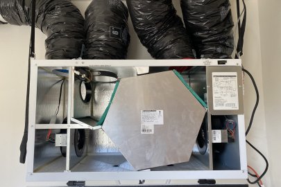 A piece of HVAC equipment mounted to a wall with exposed parts and four ducts connected to the top.