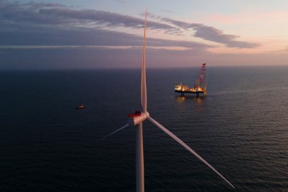 The Vole Au Vent (construction boat) installing the second wind turbine (tower section is installed) with a view from behind the completed first wind turbine (now with nacelle and blades installed). There is also a safety vessel on the left side – it was present during construction to request non-project vessel traffic to stay away from the active construction work.