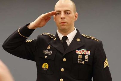 A man stands in military uniform and salutes to someone standing behind the camera