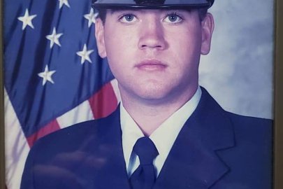 Photo of a person in military uniform infront of the American Flag.
