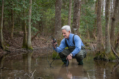A man crouches down in water and uses a device to test it