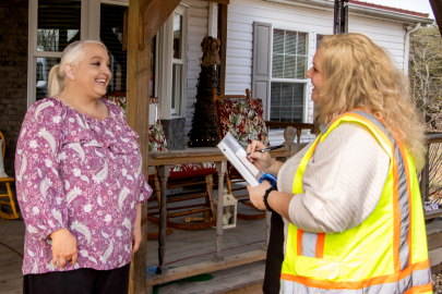 One women in a safety vest speaks to another woman in a pink patterned shirt
