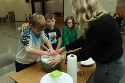 One adult and three young students perform a science experiment at a table