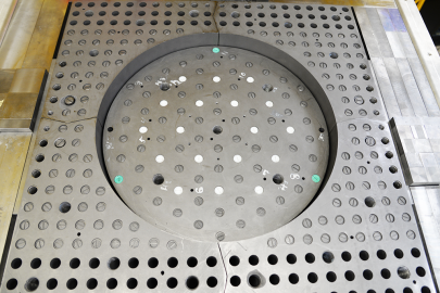 THETA experiment core, a metallic square perforated by numerous holes with a circular depression in the center.