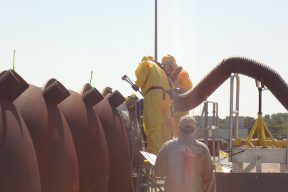 Employees in safety gear replace valves on large metal cylinders