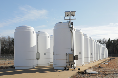 Two rows of tall white cylinders on a concrete pad with a blue sky in the background.