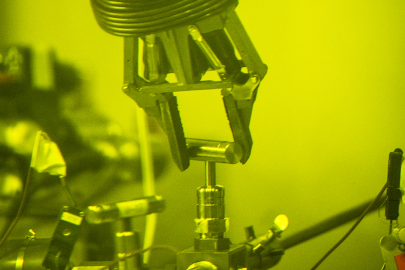 Green-tinted photo of a robotic claw holding a metal pin attached to lab equipment.
