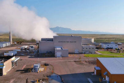 Exterior view of the Advanced Test Reactor, a tall gray building with a column of steam rising from the left side.