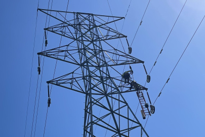 helicopter over transmission tower and lines. blue sky in background.