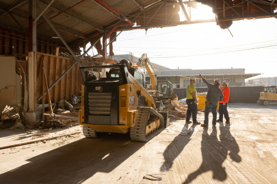 A construction vehicle outside with a few employees standing beside it