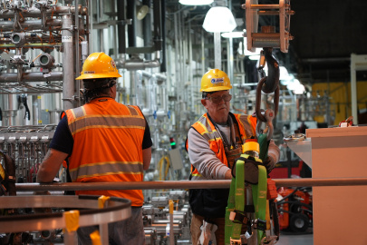Two employees in protective gear working on a rigging machine
