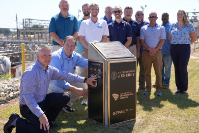A group of professionals pose for a group photo beside a large black and gold plaque