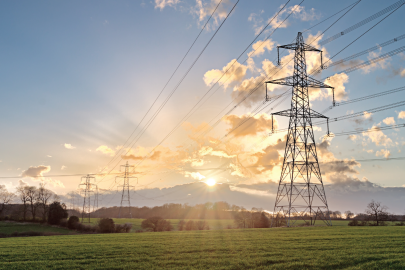 Transmission lines inside of a grassy area with cloudy skies.