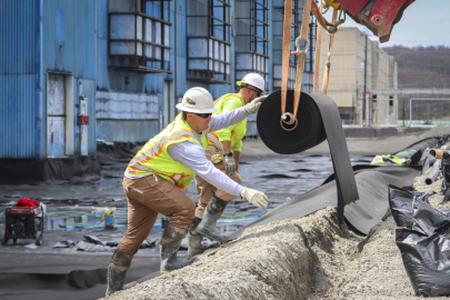Workers in safety gear rolling out a large black cylinder