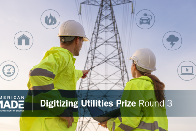 Two workers in yellow jackets and hard hats point toward a transmission line tower. 