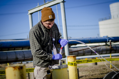 A man using a tube to take a groundwater sample from a yellow pipe