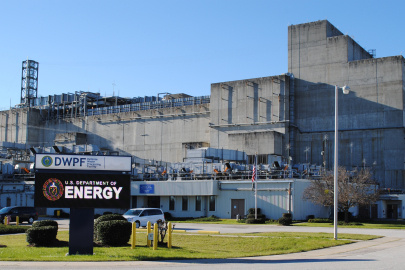 A large grey building at the Savannah River Site with a sign out front displaying the DOE seal