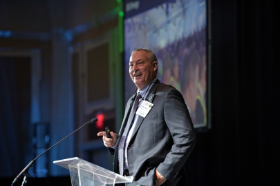 A man in a suit giving a key note address at a conference standing behind a podium