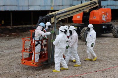 Workers in protective gear using a crane to lift a transite panel