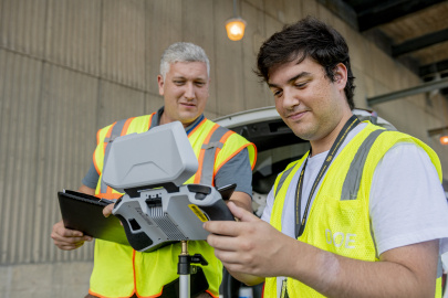 Two employees in safety vests looking at a drone controlling screen