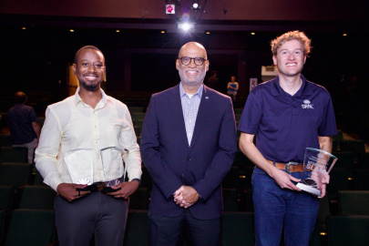 Three professionals pose for a photo and hold clear award plaques