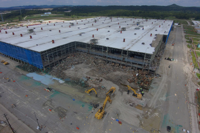 Aerial view of demolition taking place on the corner of a large building with a white roof and blue walls