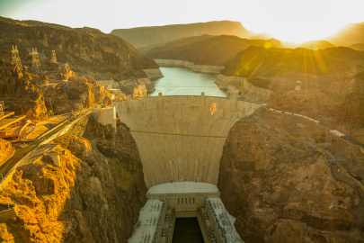 The sun rises over the hoover dam with the memorial bridge and reservoir visible in the shot