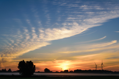 Clouds and sunset outline wind turbines on the horizon.