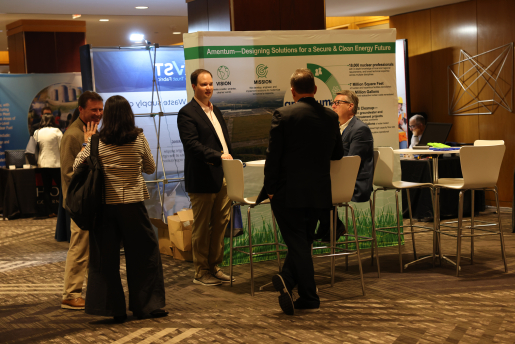 A group of five people standing and chatting with conference booths in the background