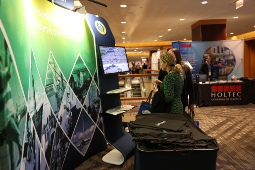 Two women view a video screen at a conference booth.