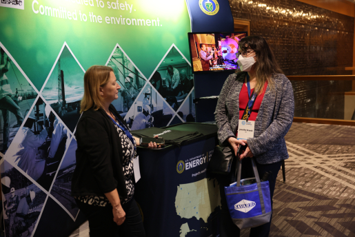 Two women stand and talk with a conference booth in the background.