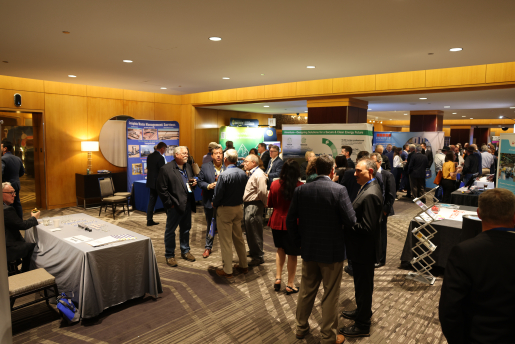 A group of business people stand and talk with conference booths in the background