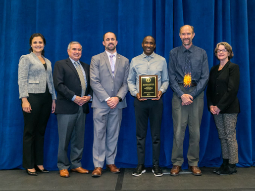 Individuals posing with an award plaque.