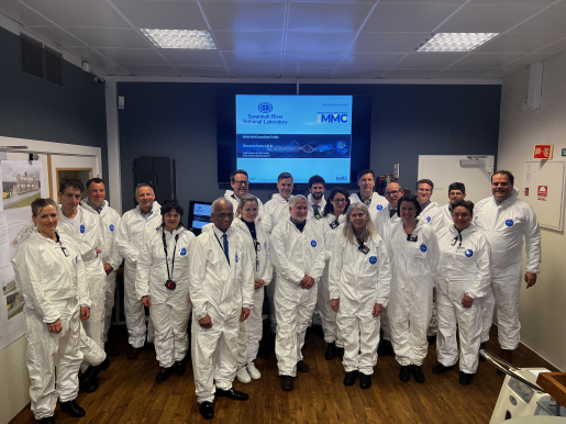 The NNSA Administrator and a group of more than 20 people all dressed in white cleanroom suits (but without head coverings).